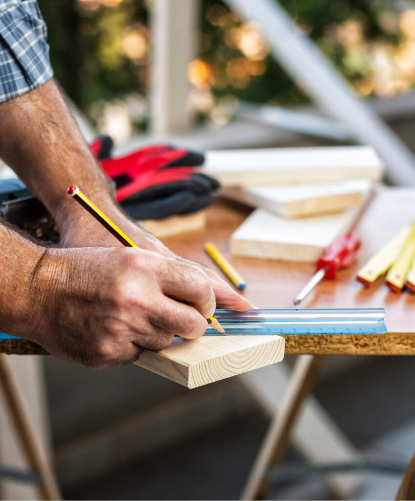 Adult craftsman carpenter with pencil and ruler tracing the cutting line on a wooden table.